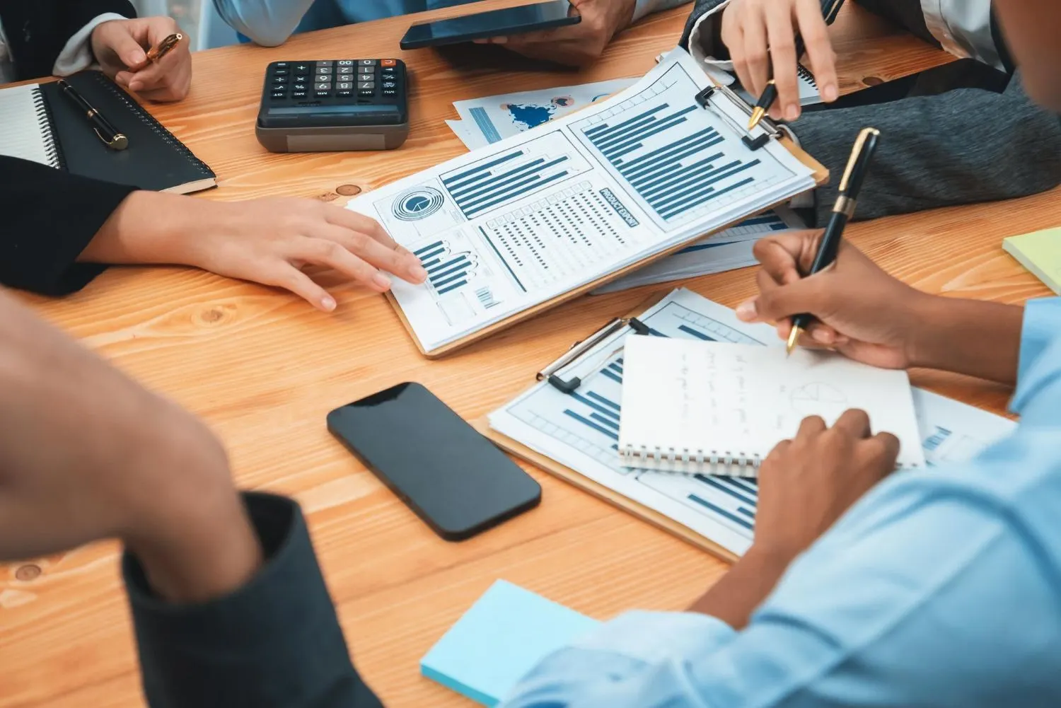 Team reviewing printed charts and notes around a wooden table